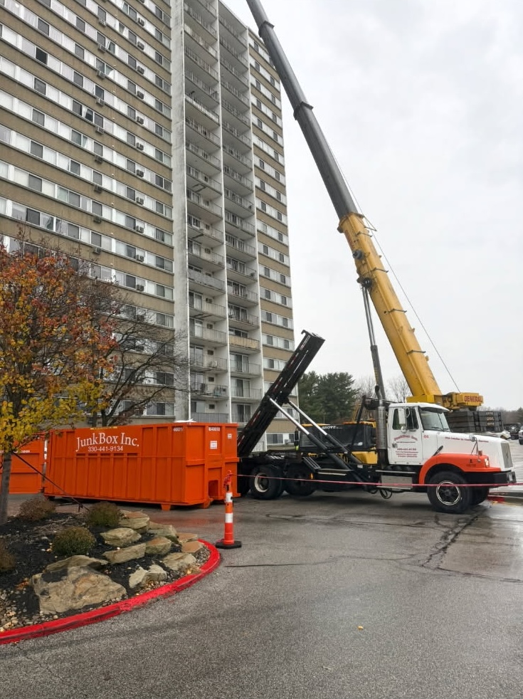 JunkBox roll-off truck hoisting a loaded orange dumpster for haul-away